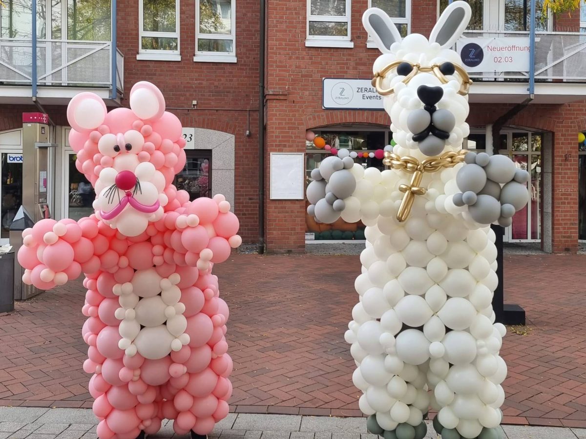 Zwei XXL-Walking-Act-Kostüme aus Ballons vor dem ZERALINO-Ladengeschäft: eine rosa Katze und ein weißes Lama mit goldener Brille und Kette