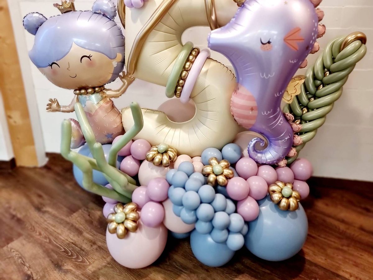Ballonstand XL im Meerjungfrau-Stil: Folienzahl in Creme mit Meerjungfrau- und Seepferdchen-Ballon, Oktopus und Seegras, auf einer Ballonbasis in Rosé, Hellblau und Flieder mit goldenen Blüten