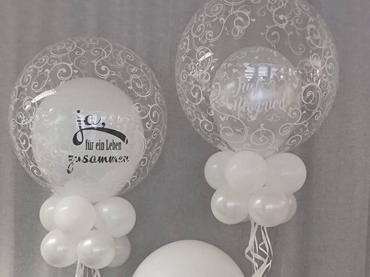 Zwei Deco Bubble Ballons zur Hochzeit mit Ornament-Print: innen ein weißer Ballon „Ja, für ein Leben zusammen“ und ein Just-Married-Ballon, darunter Ballonkränze in Weiß und Perlmutt