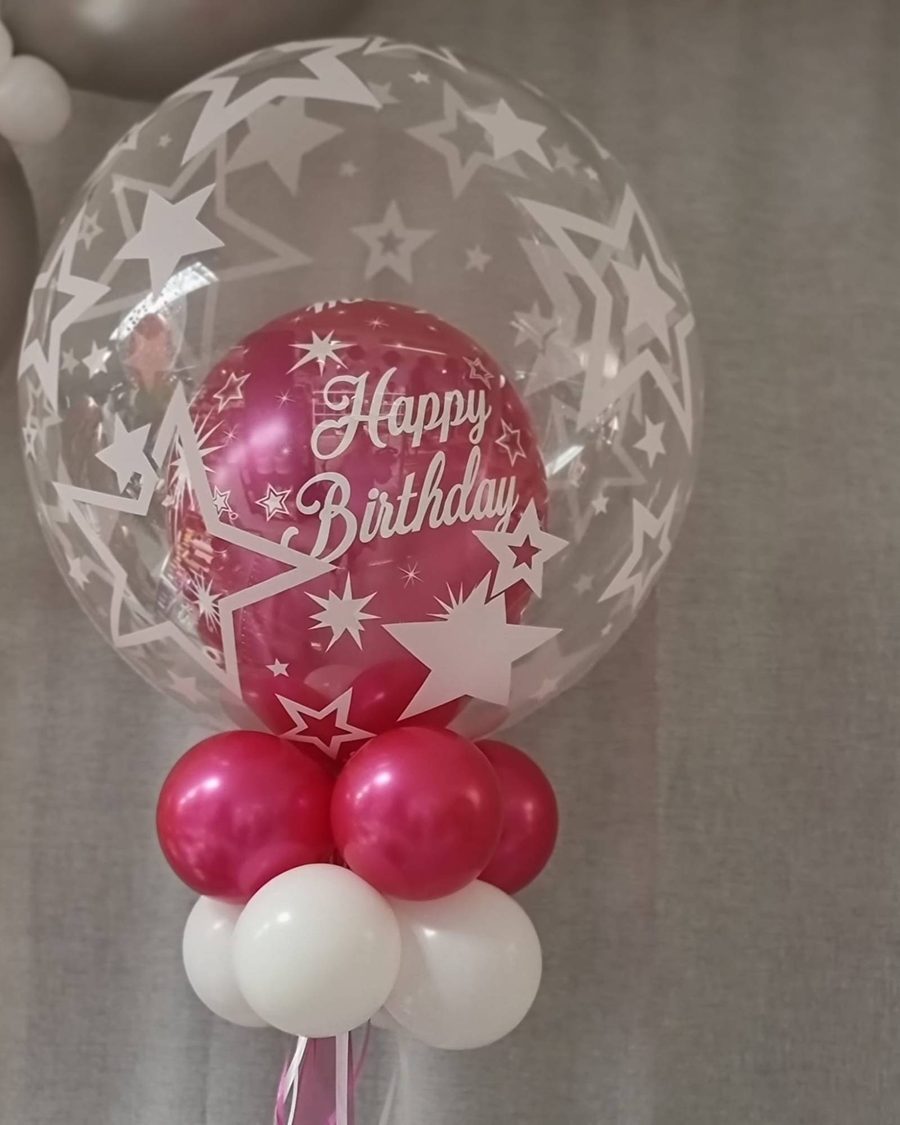 Deco Bubble mit Sternen-Print, darin ein pinker Happy-Birthday-Ballon, auf einem Ballonfuß in Pink und Weiß