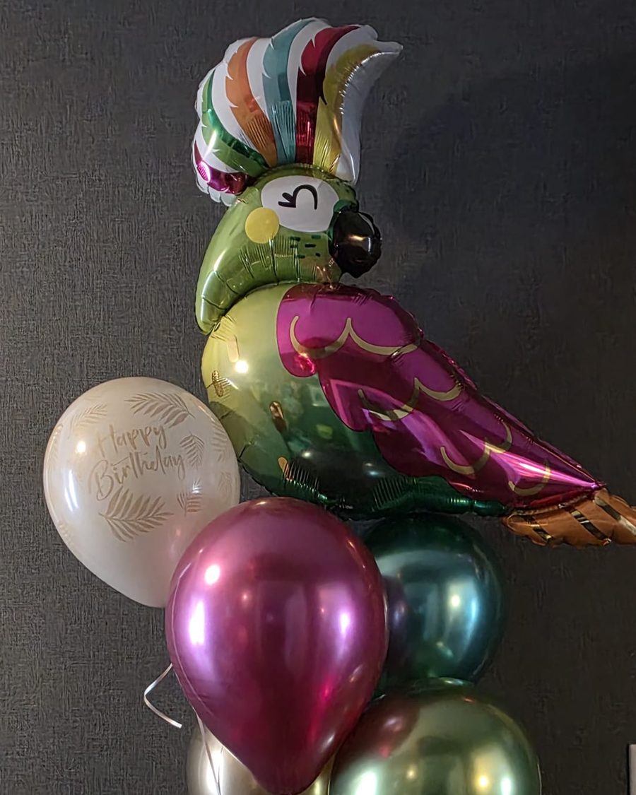 XXL-Folienballon in Form eines Papageis in Grün, Beere und Gold, darunter Chrom-Ballons und ein Happy-Birthday-Ballon