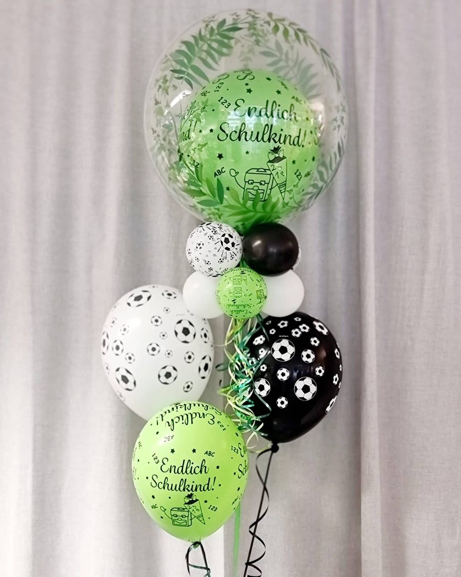 Bubble mit Blätter-Print und grünem Innenballon „Endlich Schulkind!“, dazu Ballons mit Fußball-Motiv in Schwarz und Weiß