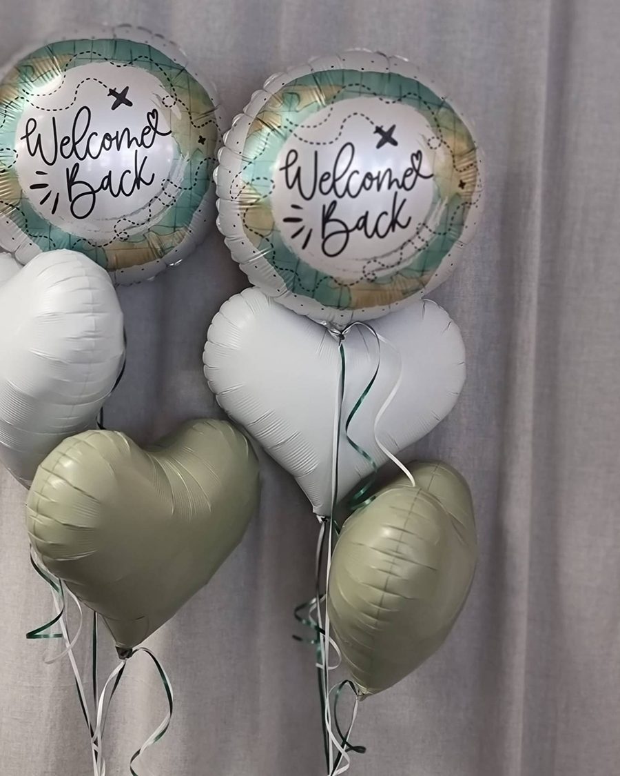 Zwei Folienballons „Welcome Back“ mit Landkarten-Motiv, dazu Herzballons in Weiß und Salbei