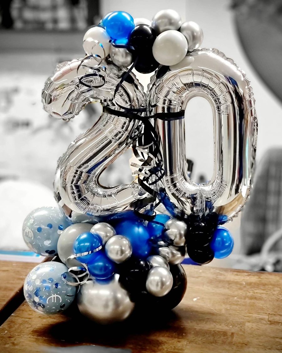 Zahlenstand „20“ aus silbernen Folienzahlen auf einem Ballonfuß in Blau, Silber und Schwarz